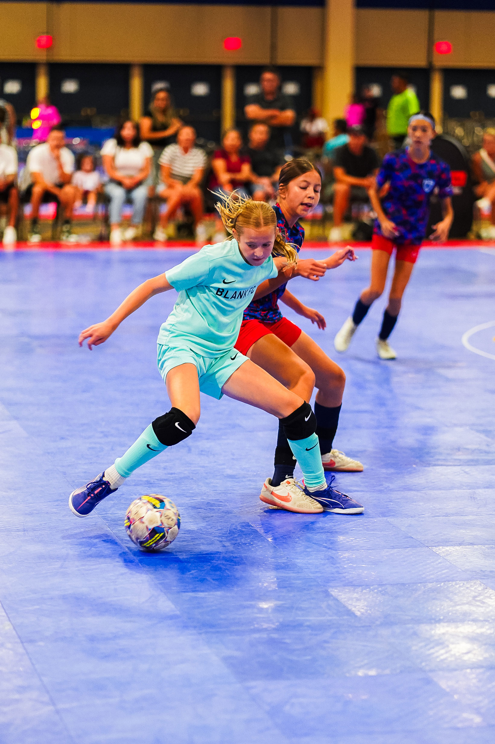 Two young girls working for control of the futsal ball on court